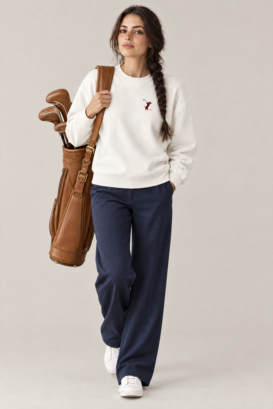Woman carrying a tan leather golf bag in the white Swing dachshund golf sweatshirt and navy wide-leg trousers. Color: White