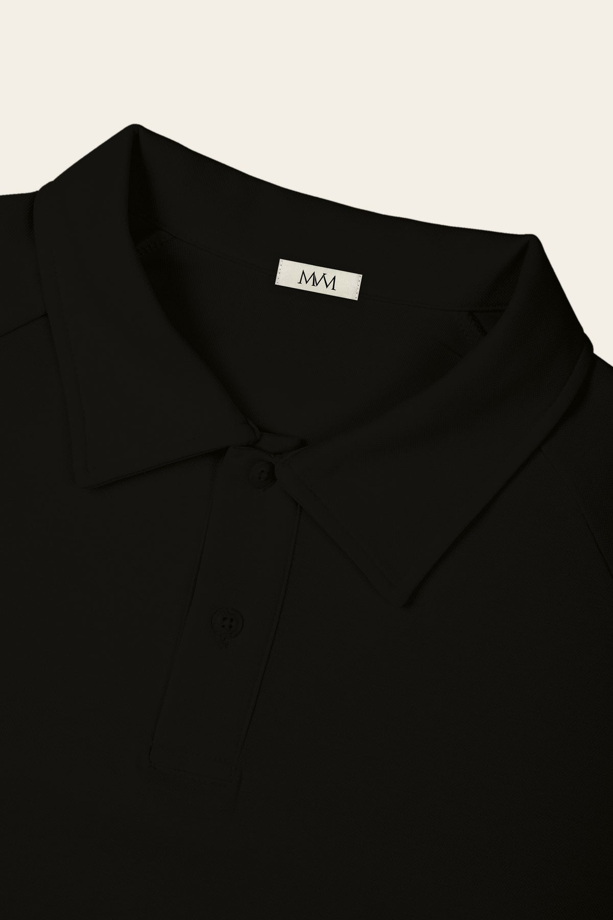 Close-up of the collar and two-button placket of the black golf polo with the MVM woven neck label. Color: Black