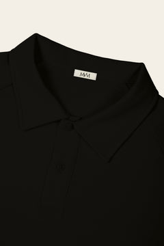 Close-up of the collar and two-button placket of the black golf polo with the MVM woven neck label. Color: Black