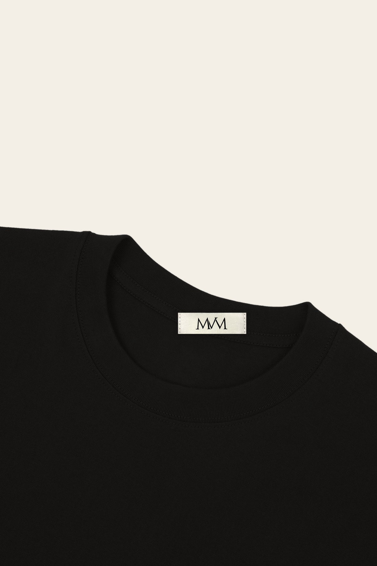 Close-up of the ribbed crew neck of the black golf t-shirt with the MVM woven neck label. Color: Black