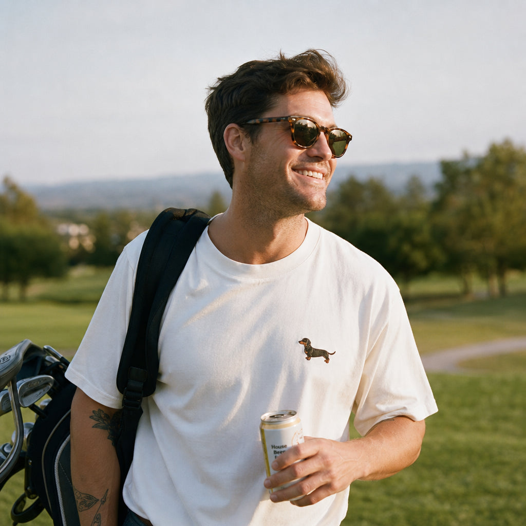 Man with sunglasses and a white t-shirt holding a can on a grassy field