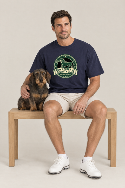 Man sitting on a bench with a wire-haired dachshund in the navy Low Center of Gravity Club Dachshund Golf Tee. Color: Navy