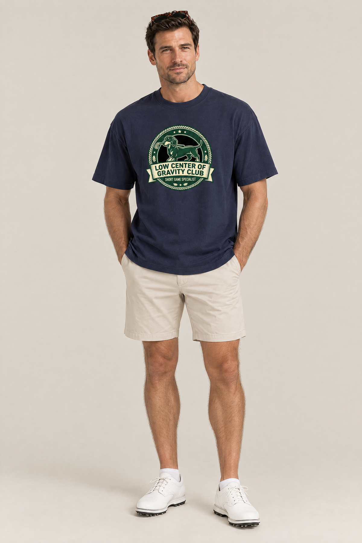Man wearing the Low Center of Gravity Club Dachshund Golf Tee in navy with stone golf shorts and sunglasses on his head. Color: Navy