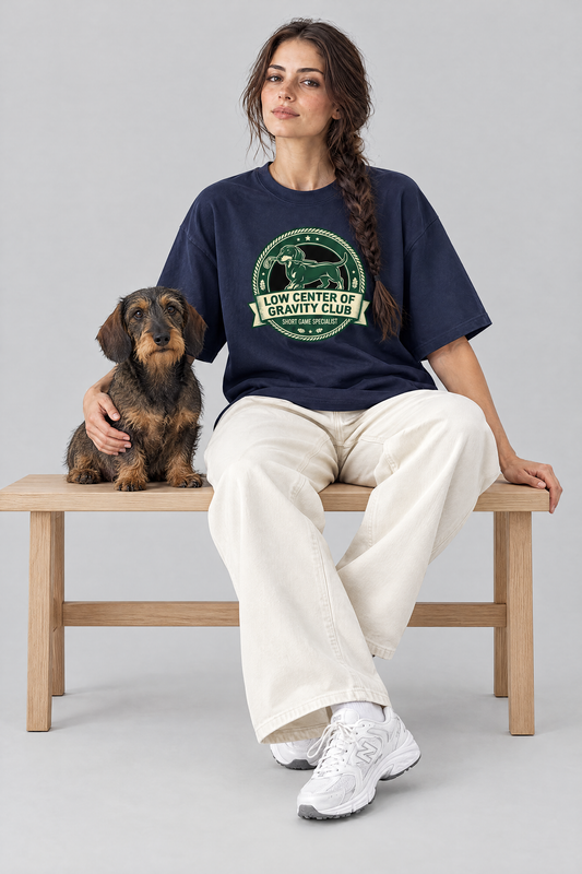 Woman sitting on a bench with a wire-haired dachshund in the navy Low Center of Gravity Club Dachshund Golf Tee. Color: Navy