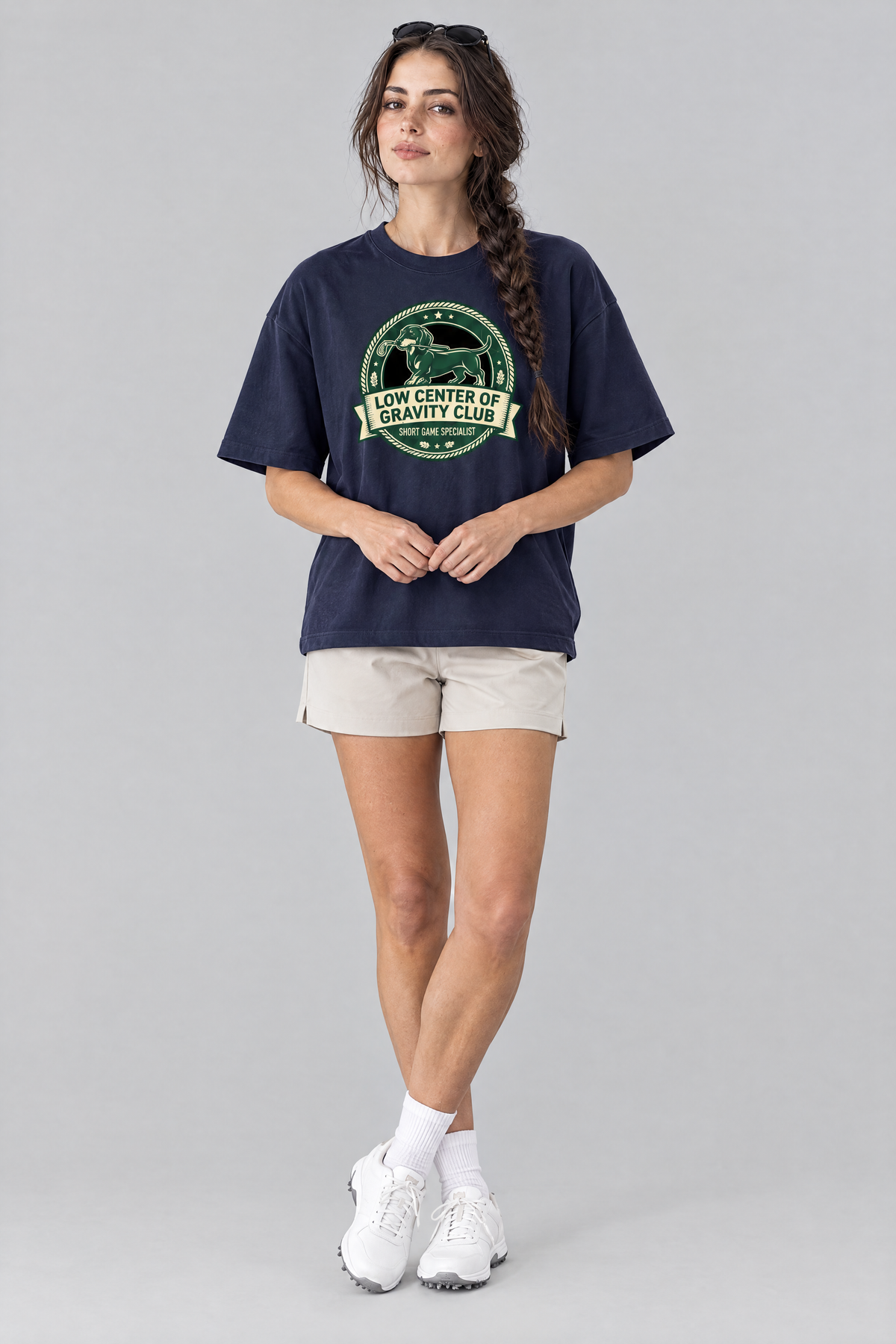 Woman wearing the Low Center of Gravity Club Dachshund Golf Tee in navy with stone golf shorts and sunglasses on her head. Color: Navy