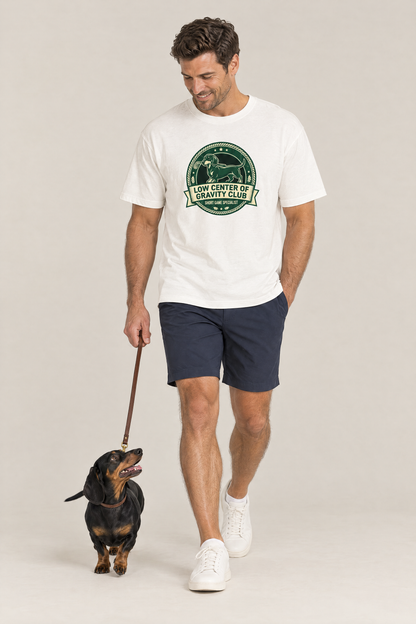 Man walking a dachshund on a leash in the white Low Center of Gravity Club Dachshund Golf Tee. Color: White