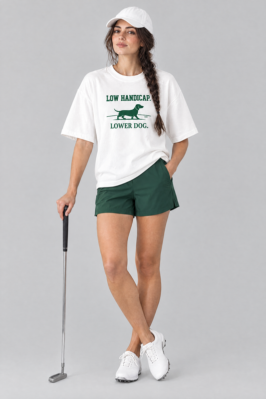 Woman wearing the Low Handicap Dachshund Golf Tee in white with green golf shorts and a white cap, holding a putter. Color: White