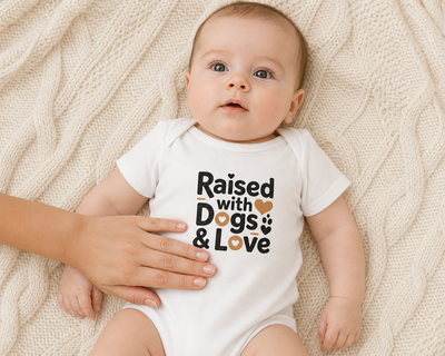 Baby wearing a white onesie with 'Raised with Dogs & Love' text, lying on a textured beige surface.