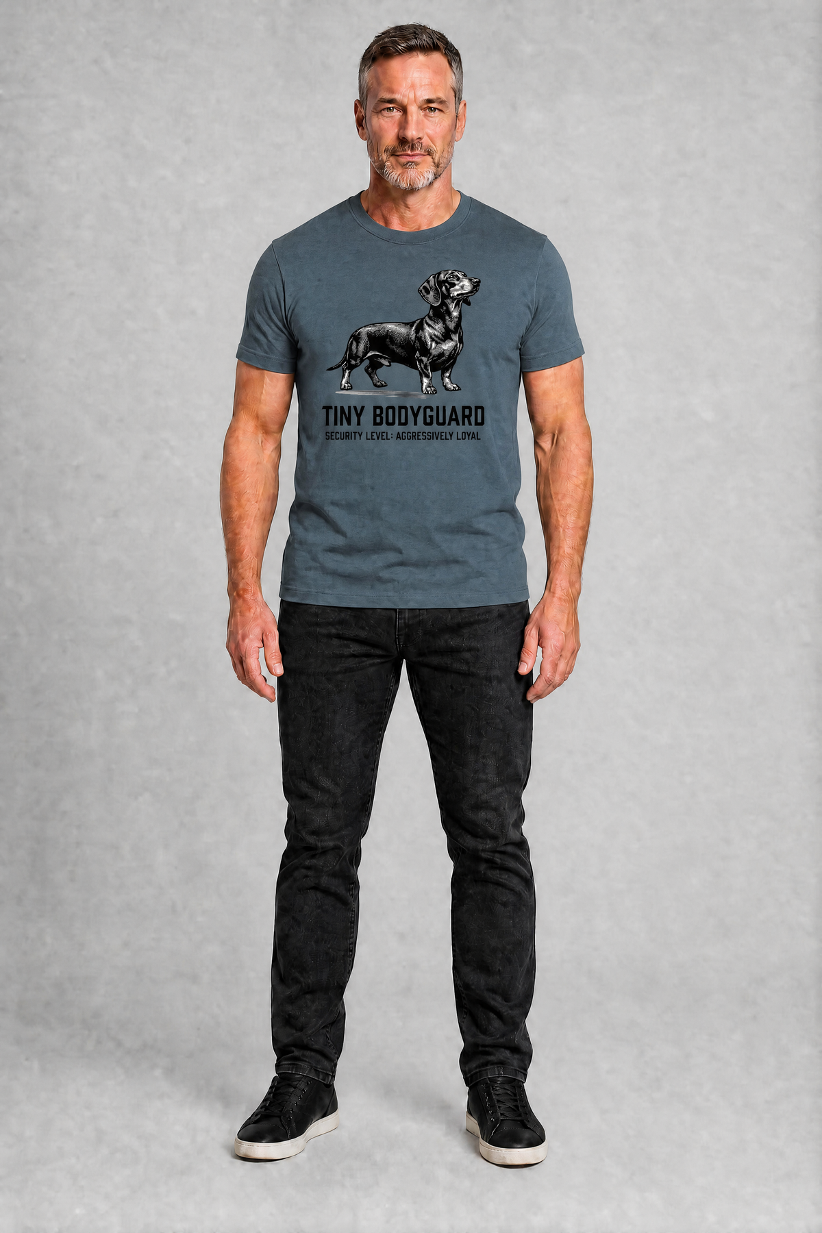 Man wearing a gray t-shirt with a graphic and text, standing against a plain background