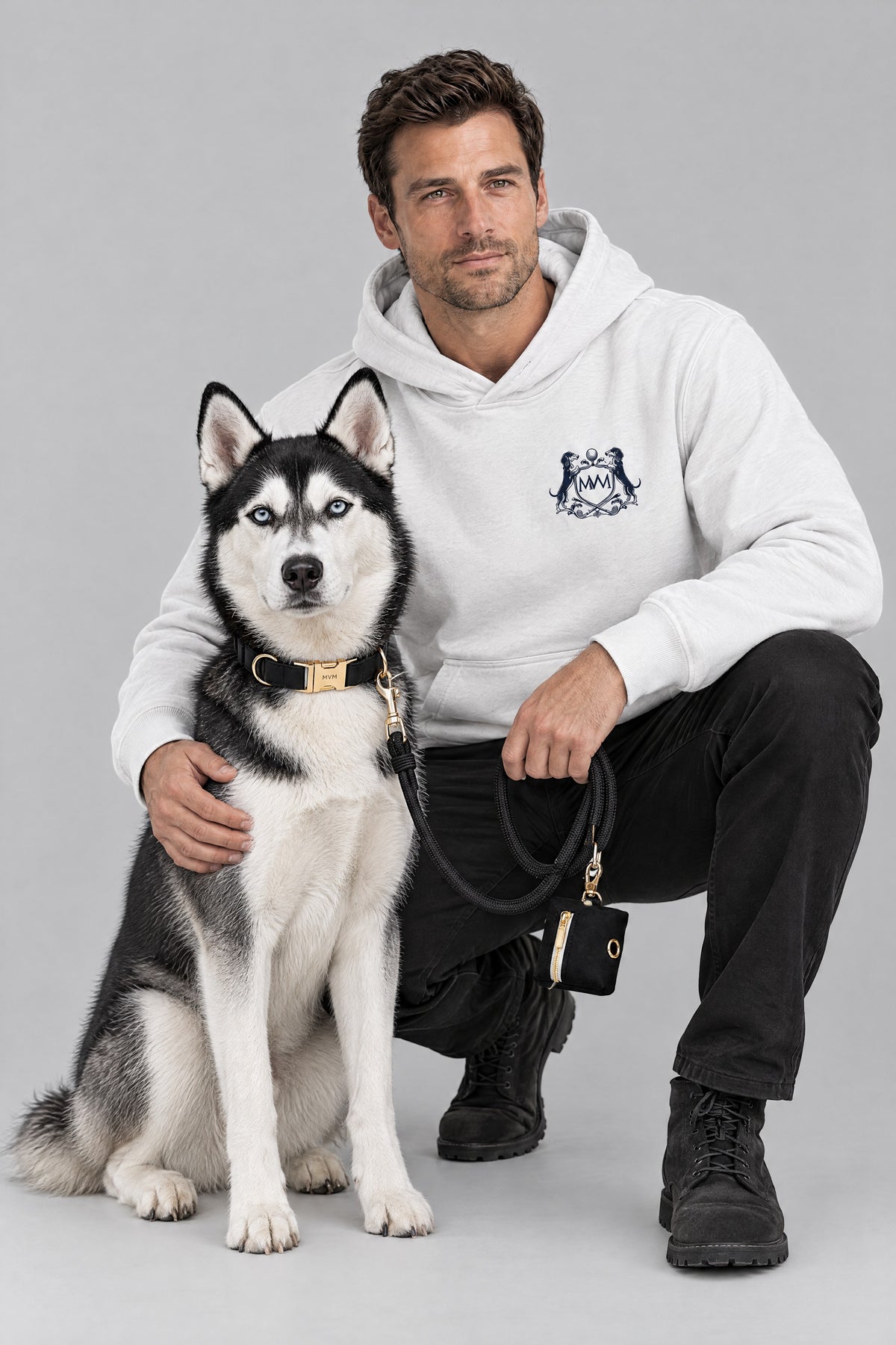 Man in the white Club Crest hoodie crouching with a Siberian Husky wearing the black MVM Evergreen set