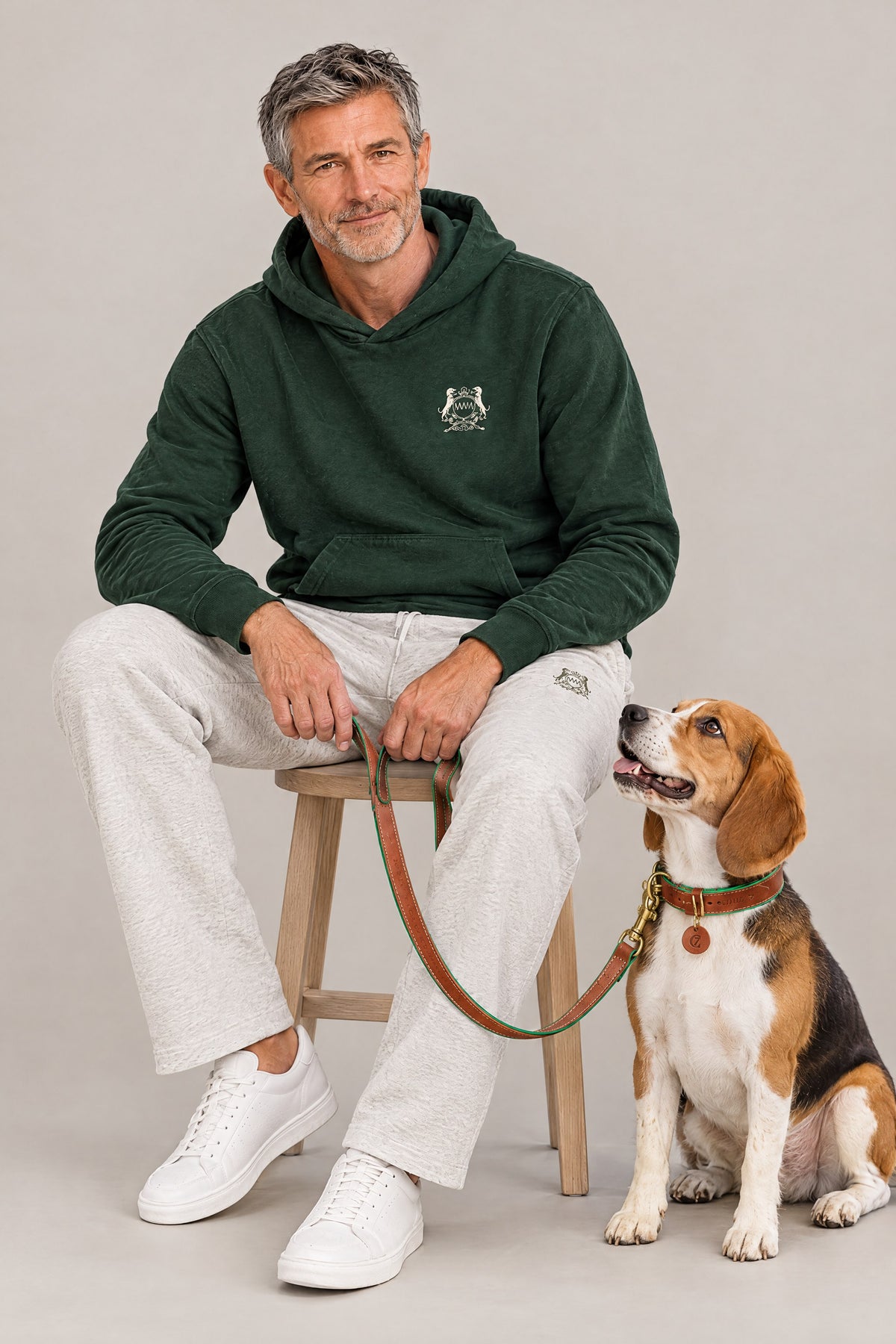 Man in the blackish green Club Crest hoodie seated next to a beagle wearing the cognac green Cloud 7 Kings Park collar and leash
