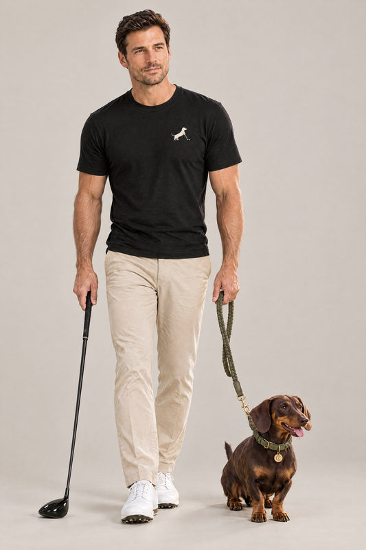 Man in the black Putting dachshund golf tee holding a golf club next to a dachshund wearing the olive Cloud 7 Ravello collar and leash