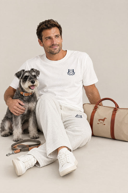 Man in the white Club Crest tee and oat gray sweatpants sitting with a Miniature Schnauzer wearing the Cloud 7 Tivoli Greige collar