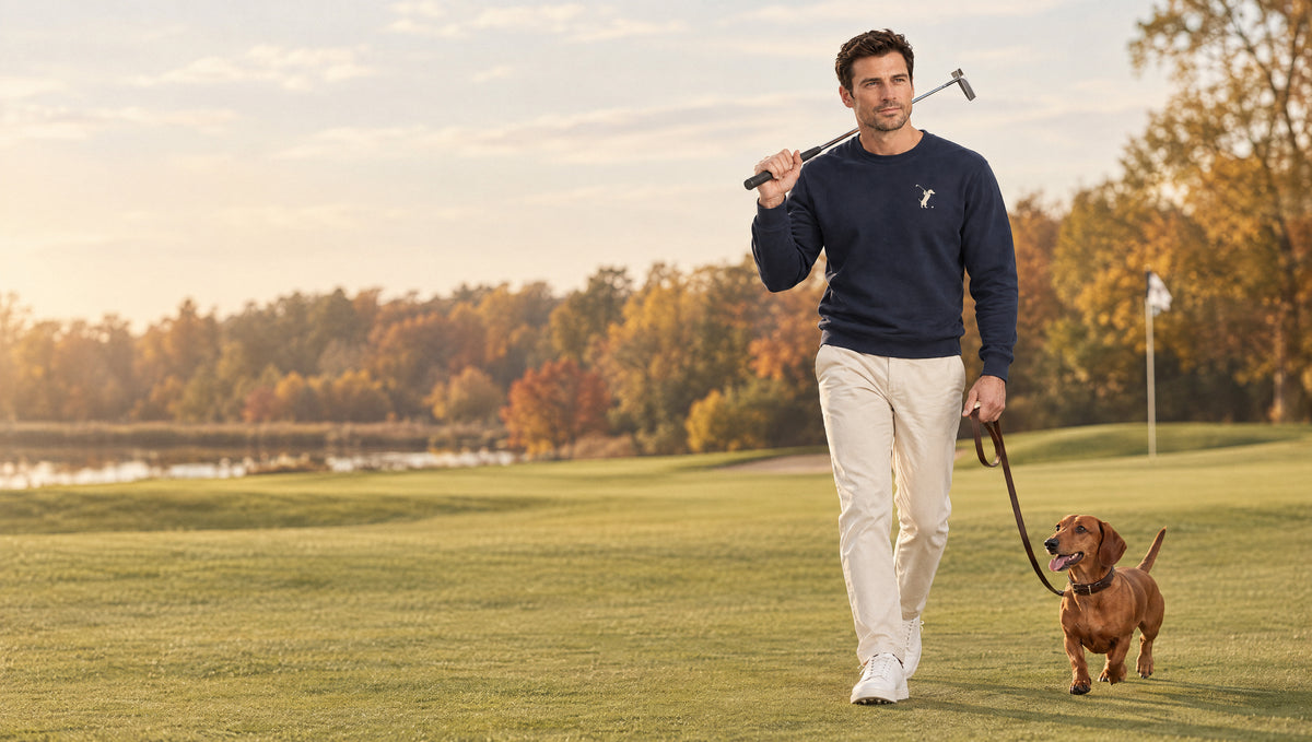 Man in the navy Swing dachshund golf sweatshirt walking his dachshund across a fairway with a putter on his shoulder
