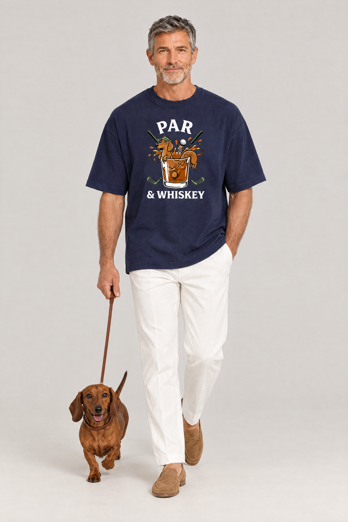 Man walking a red dachshund on a leash in the navy Par & Whiskey Dachshund Golf Tee. Color: Navy