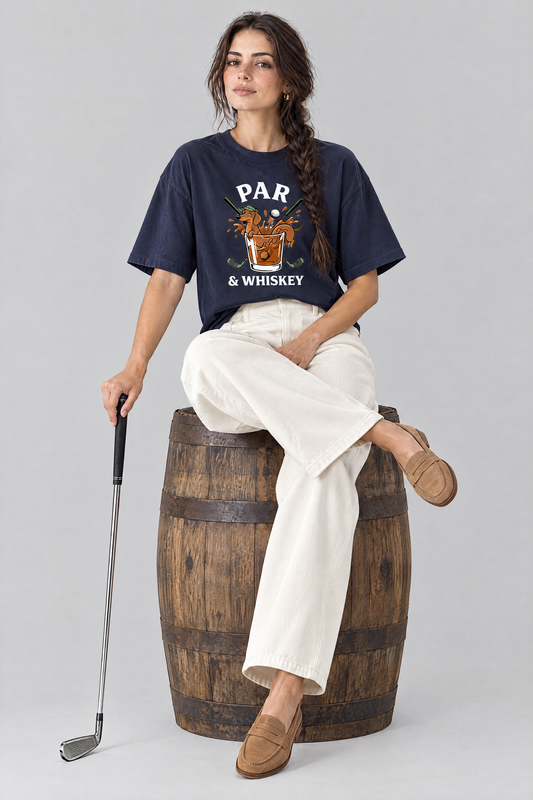 Woman sitting on a whisky barrel with a golf iron in the navy Par & Whiskey Dachshund Golf Tee and cream wide-leg trousers. Color: Navy