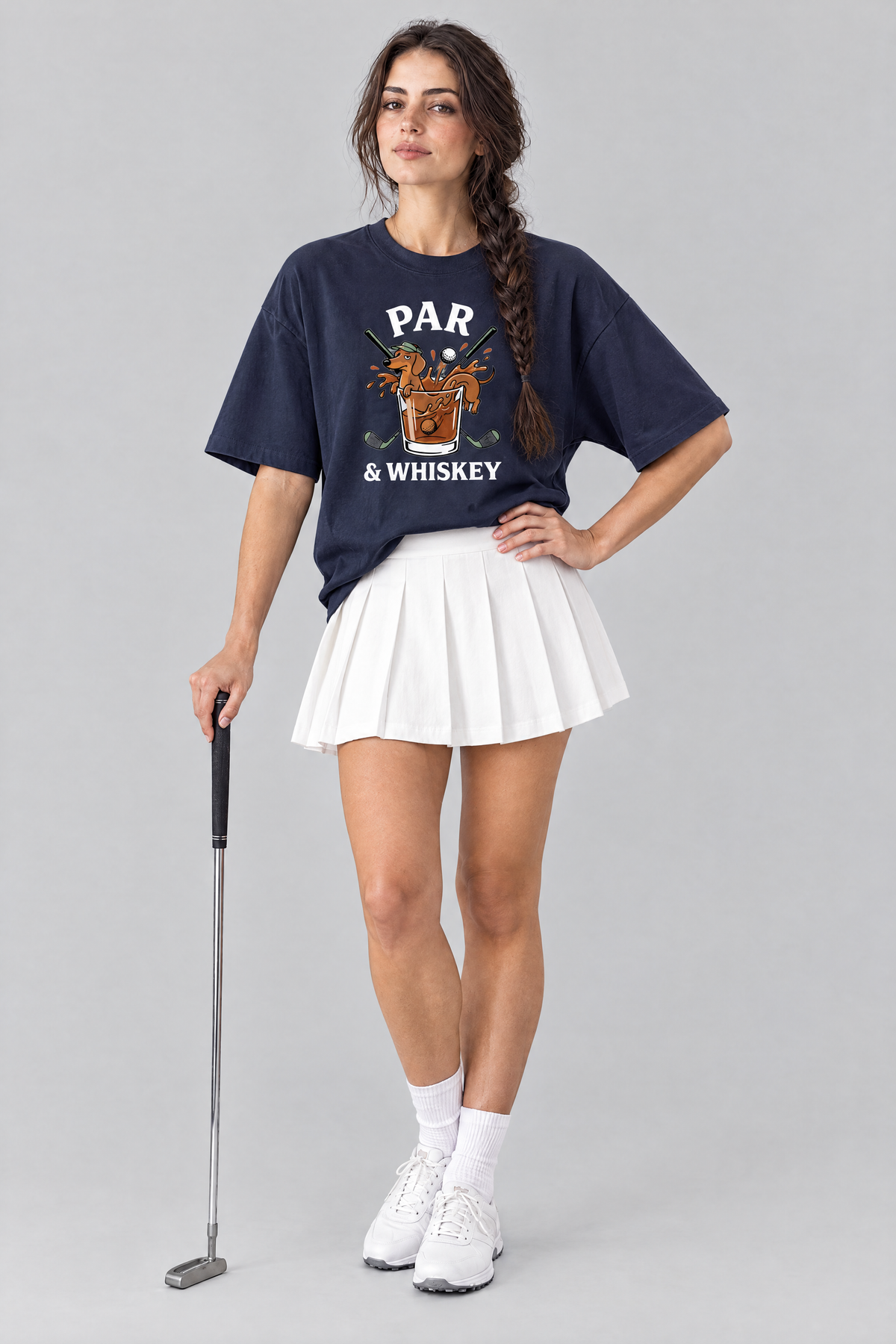Woman wearing the Par & Whiskey Dachshund Golf Tee in navy with a white pleated skirt, holding a putter. Color: Navy