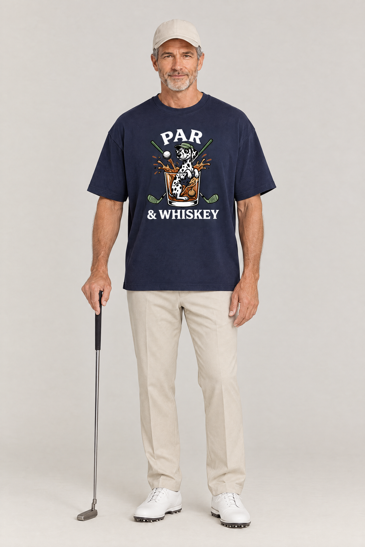 Man holding a golf putter in the navy Par & Whiskey Dalmatian Golf Tee with stone trousers. Color: Navy