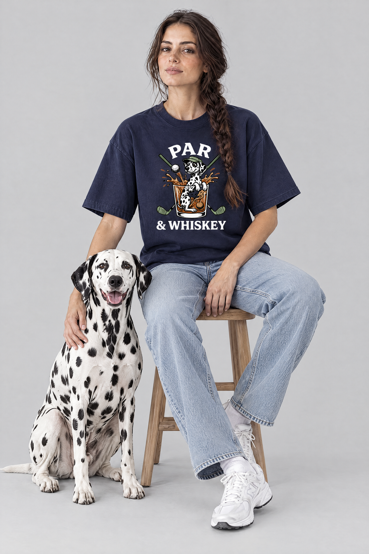 Woman sitting on a stool with a Dalmatian dog in the navy Par & Whiskey Dalmatian Golf Tee. Color: Navy