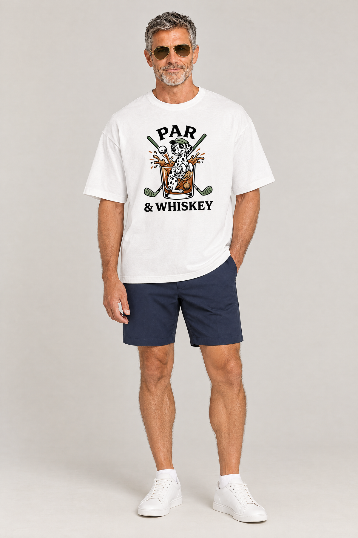 Man wearing the Par & Whiskey Dalmatian Golf Tee in white with navy golf shorts and aviator sunglasses. Color: White