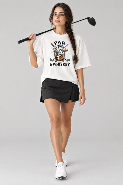 Woman walking with a golf driver on her shoulder in the white Par & Whiskey Dalmatian Golf Tee and a black golf skort. Color: White
