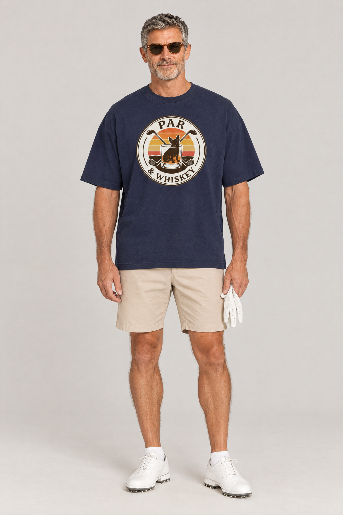 Man wearing the Par & Whiskey French Bulldog Badge Golf Tee in navy with beige golf shorts and sunglasses. Color: Navy