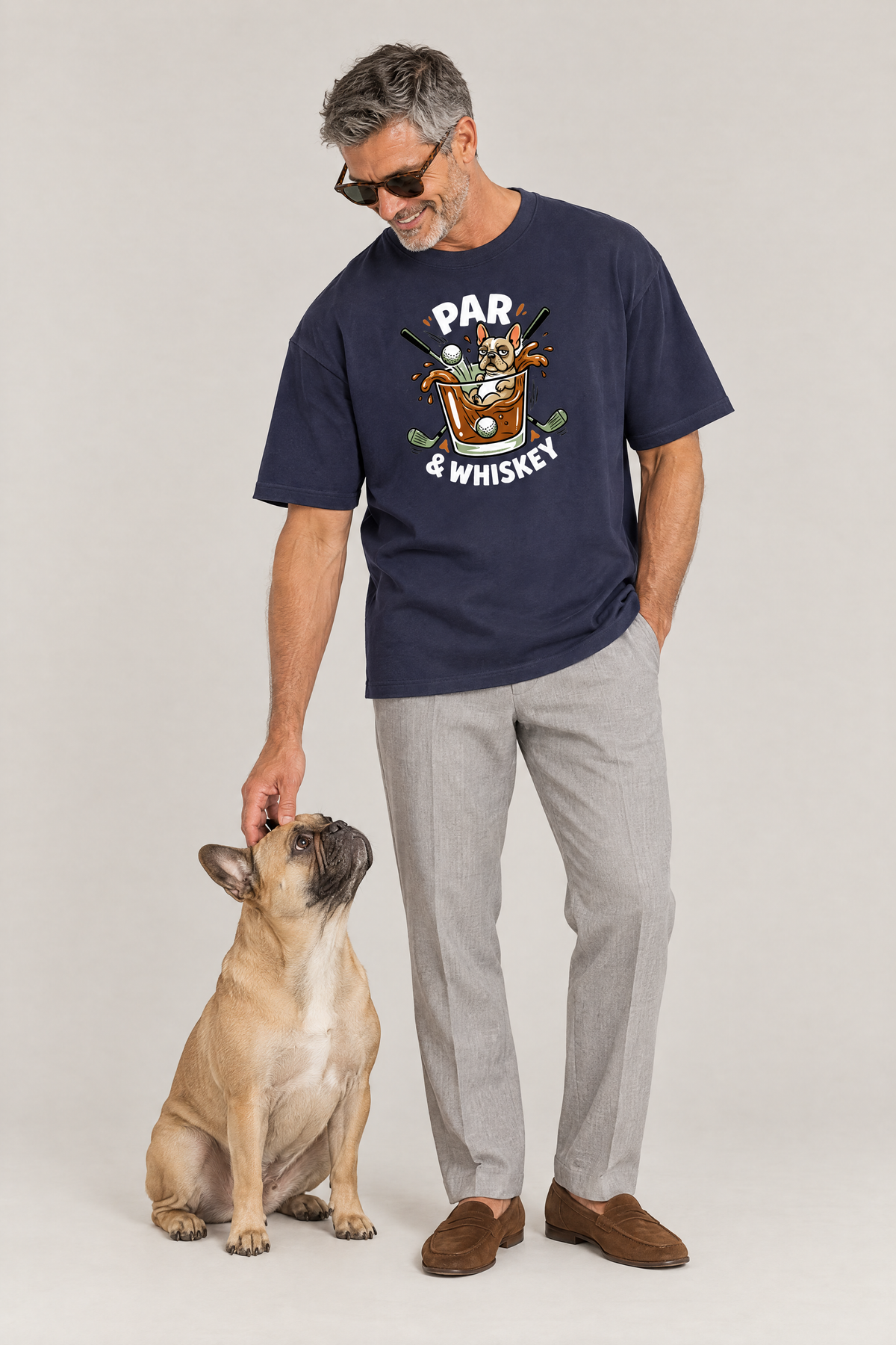 Man wearing the Par & Whiskey French Bulldog Splash Golf Tee in navy with a French bulldog sitting at his feet. Color: Navy