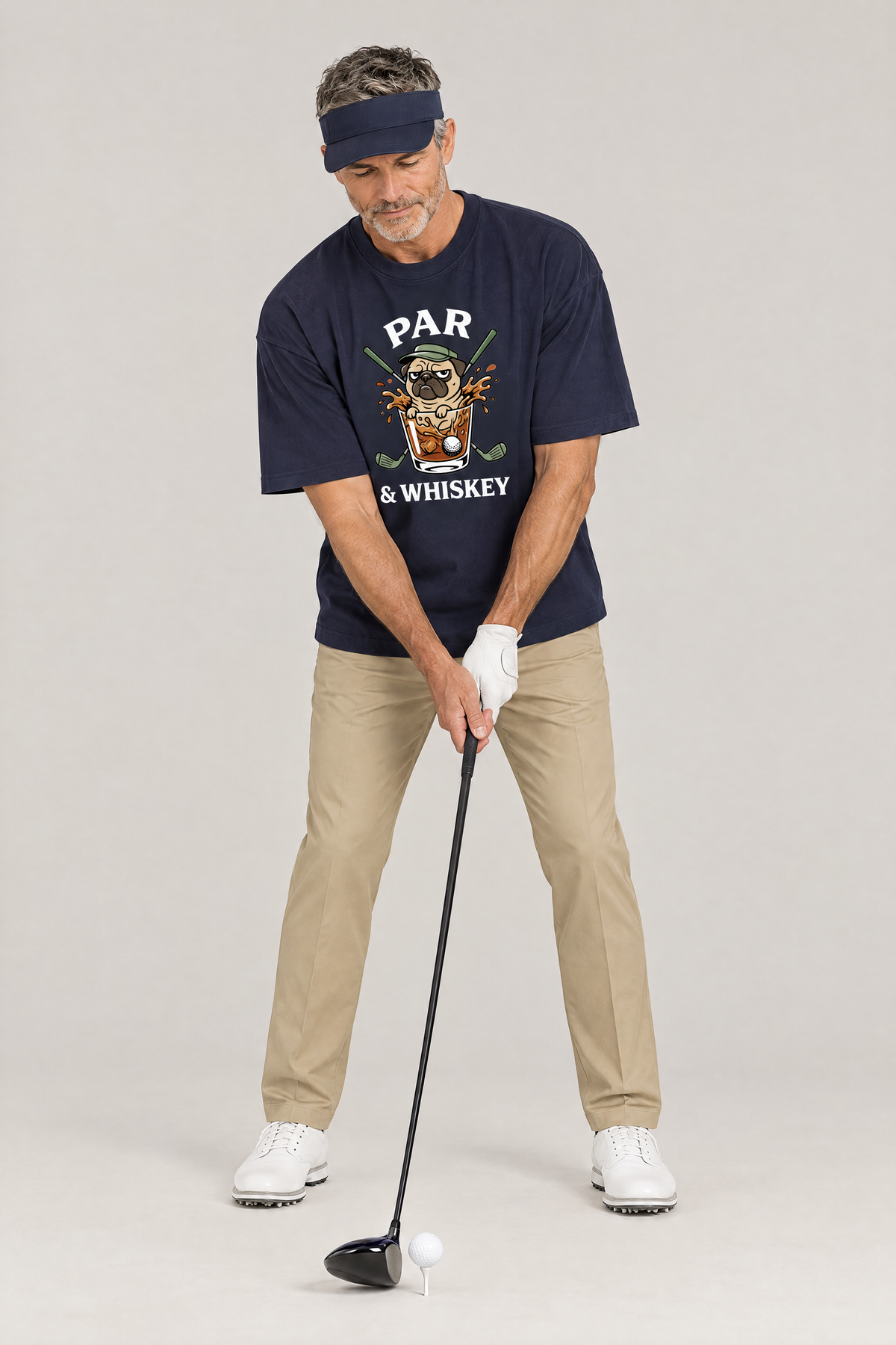 Man addressing the ball with a driver in the navy Par & Whiskey Pug Golf Tee. Color: Navy