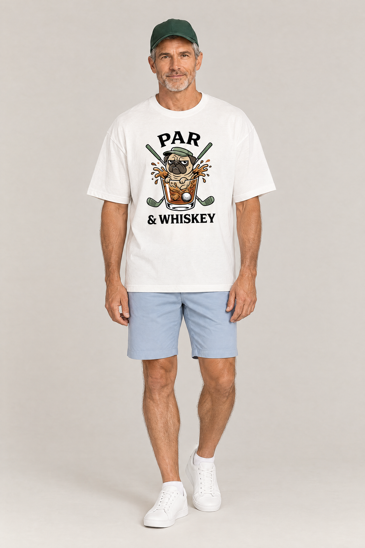 Man wearing the Par & Whiskey Pug Golf Tee in white with light blue golf shorts and a green cap. Color: White