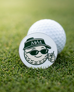 19th Hole golf ball marker in forest green and cream print on a putting green next to a golf ball