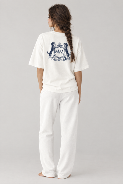 Back view of a woman in white Club Crest sweatpants and a white tee with a large crest on the back