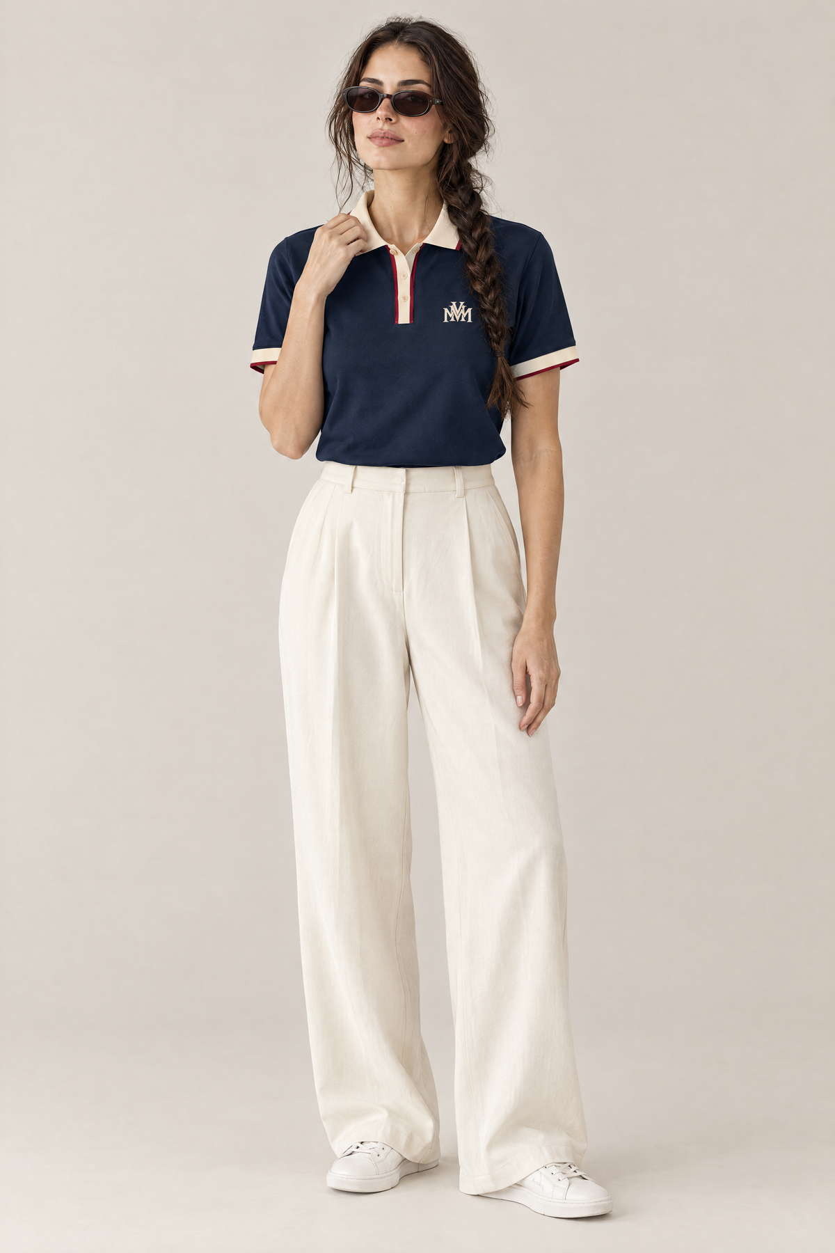 Woman wearing the navy Club Crest color block polo with apricot trim, cream wide-leg trousers and sunglasses. Color: Navy Blue with Apricot
