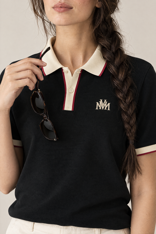 Woman holding sunglasses at the collar of the black Club Crest polo, close-up of the apricot monogram. Color: Black with Apricot