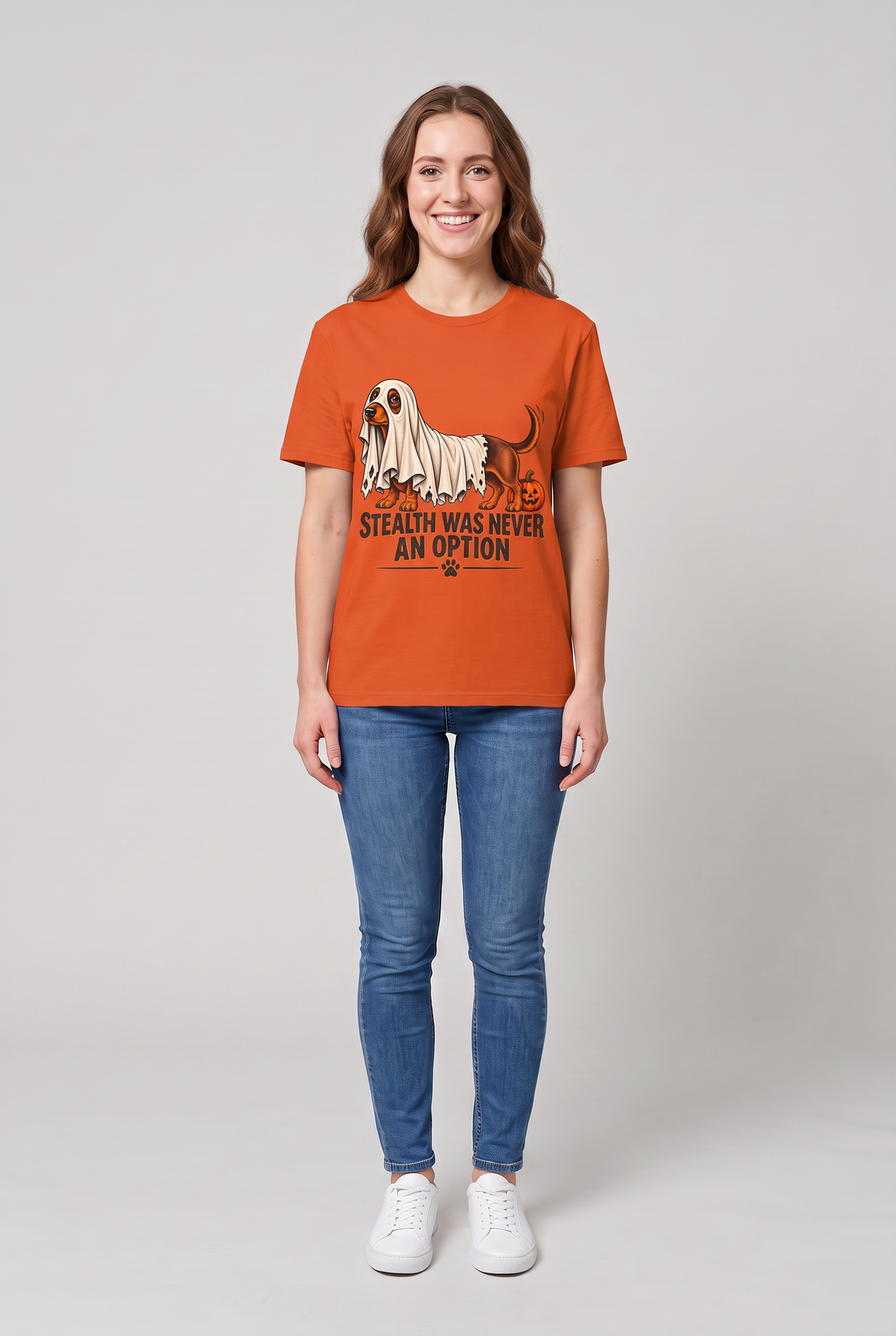 Frau trägt ein Dackel Halloween T-Shirt in Orange mit Dackel unter einem zu kurzen Gespensterlaken und dem Spruch Stealth Was Never An Option, Vorderansicht