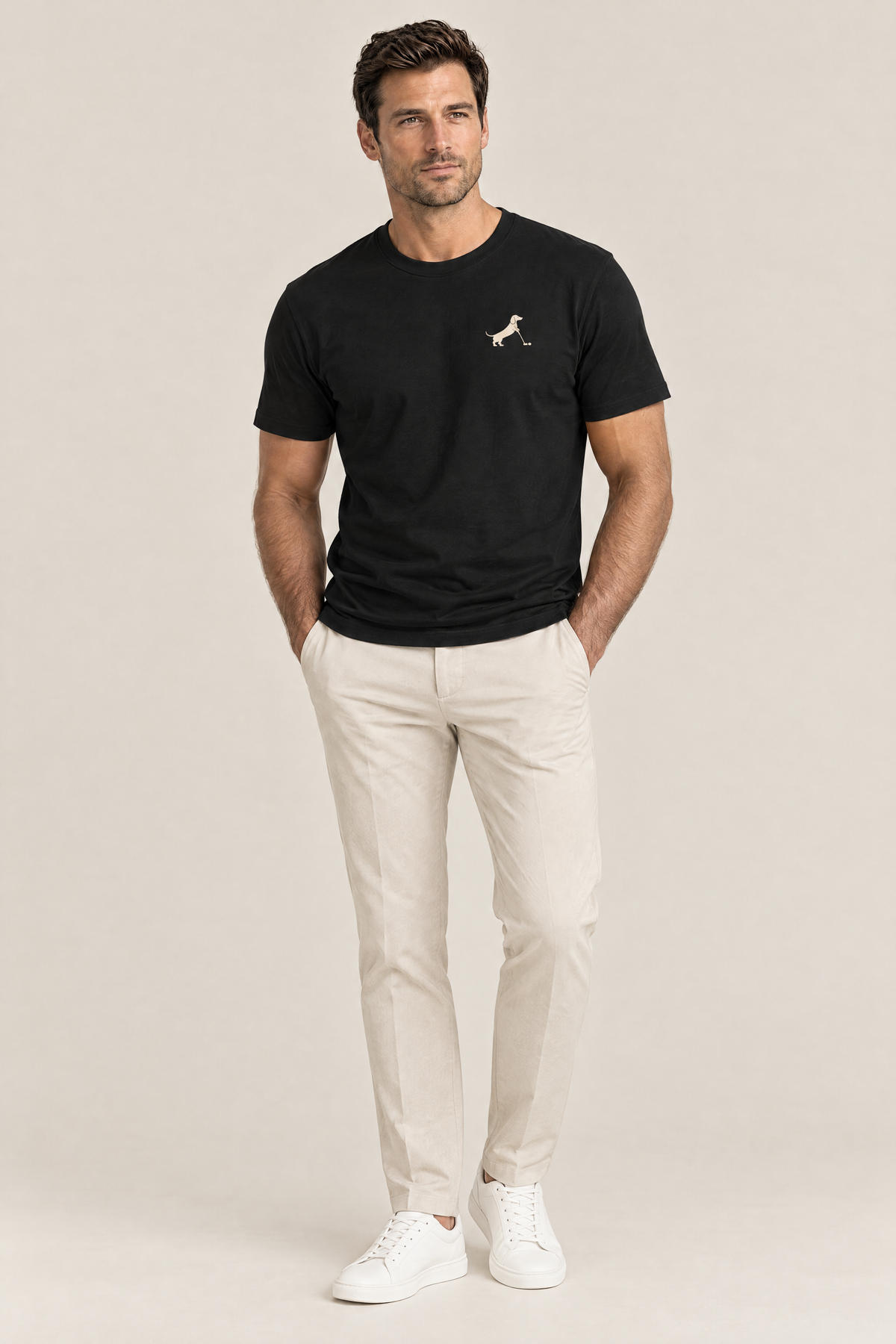 Man wearing black Putting dachshund golf t-shirt with small cream chest print, hands in pockets of beige golf trousers, full-body studio look. Color: Black
