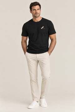 Man wearing black Putting dachshund golf t-shirt with small cream chest print, hands in pockets of beige golf trousers, full-body studio look. Color: Black