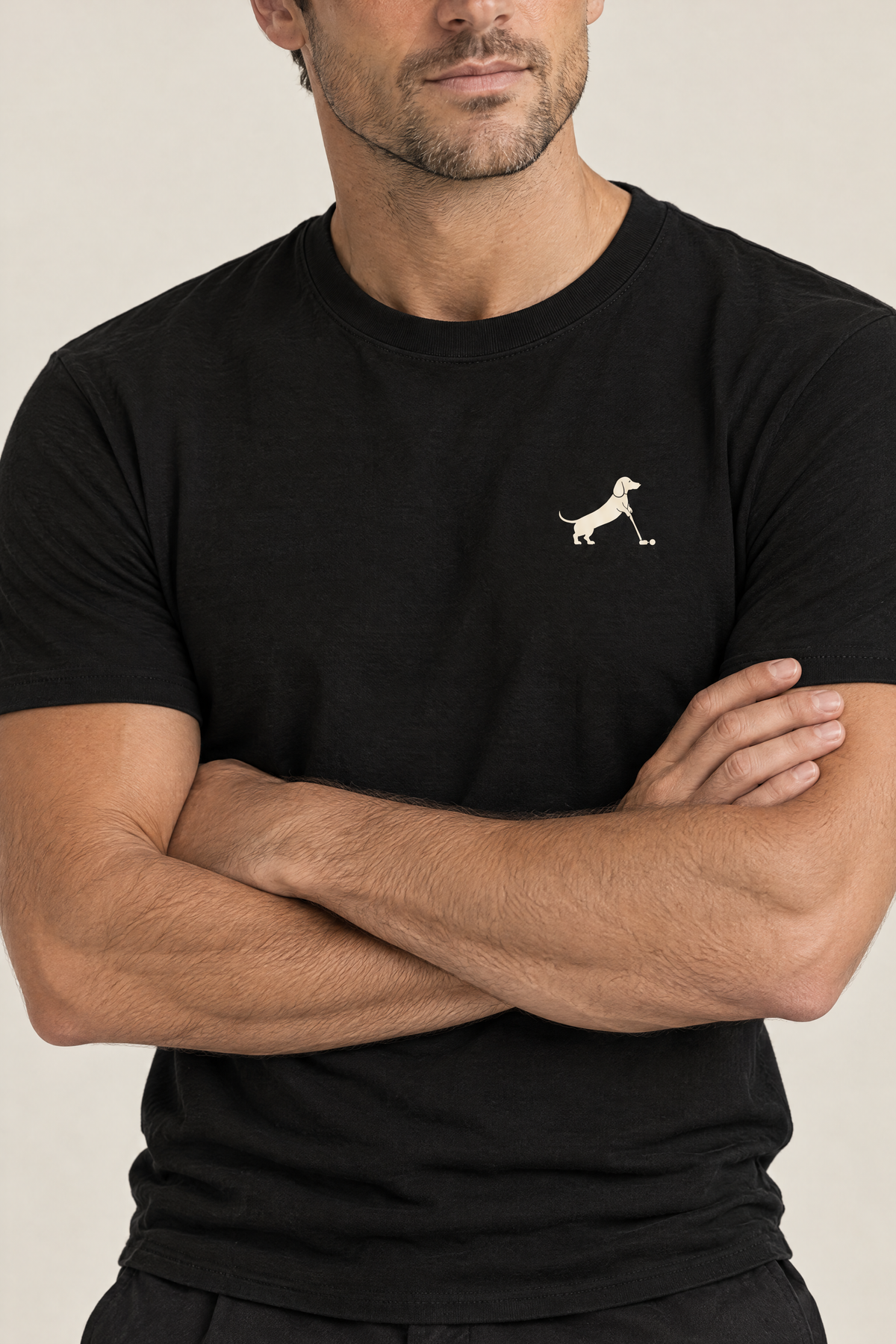 Close-up of man with crossed arms wearing black Putting dachshund golf t-shirt, chest print detail. Color: Black