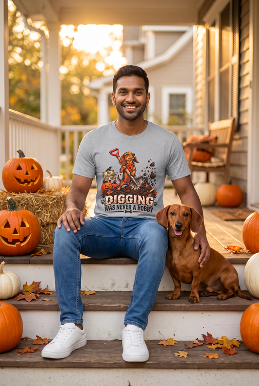Man in a sport grey funny dachshund Halloween t-shirt with a digging wiener dog and the text Digging Was Never A Hobby sitting on a fall porch with a red dachshund and pumpkins