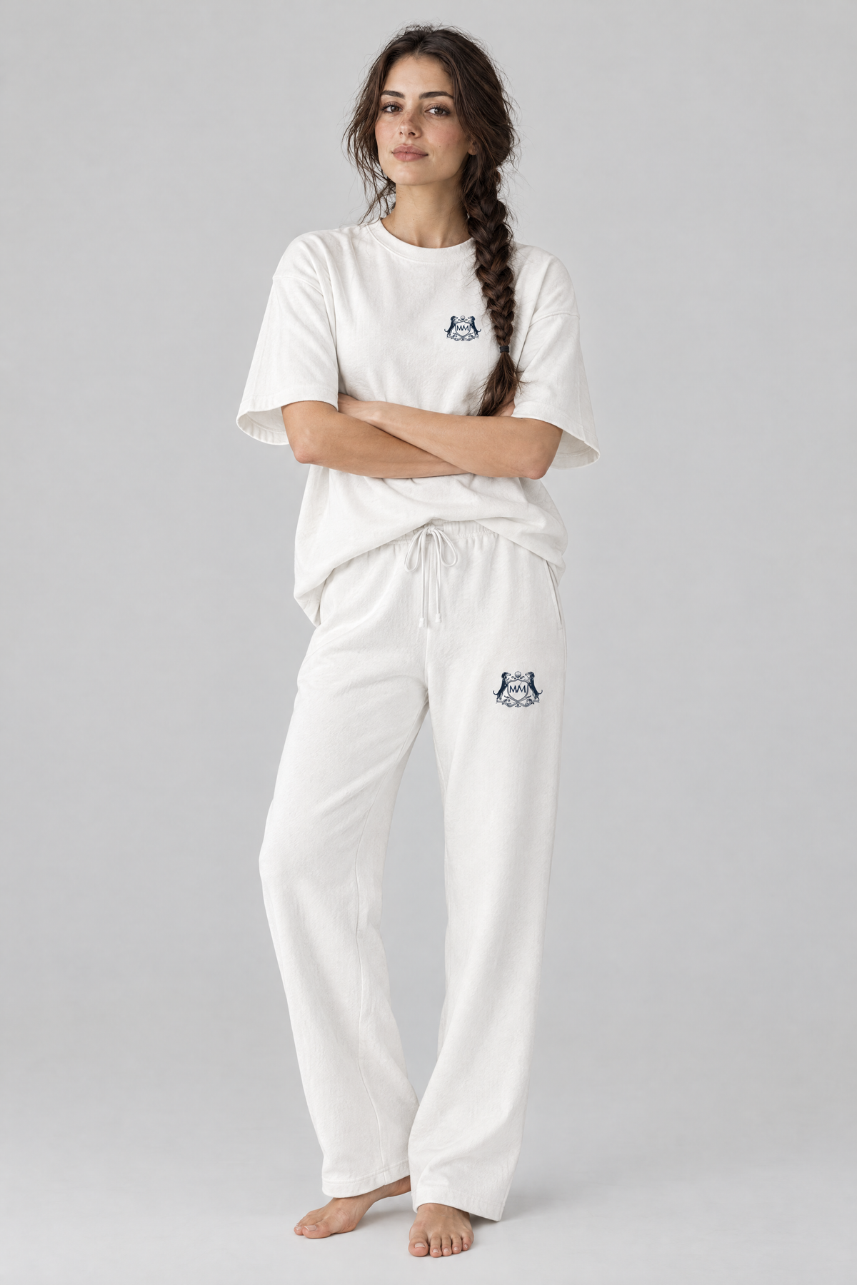 Woman standing with arms crossed in white Club Crest sweatpants and a white tee, full body, tone-on-tone set