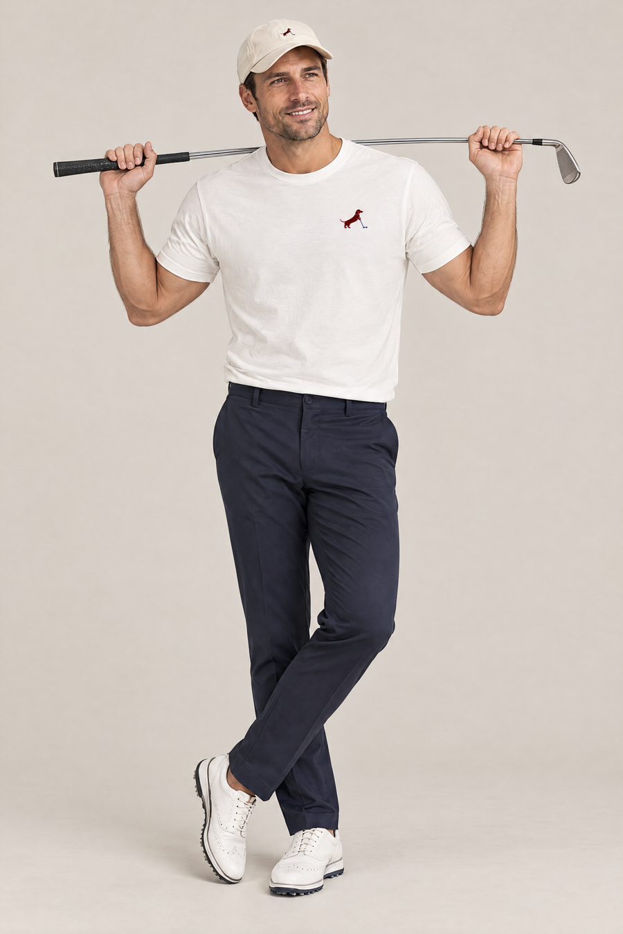 Smiling man in cream golf cap and white Putting dachshund golf t-shirt holding a golf club behind his shoulders, full-body studio look. Color: White