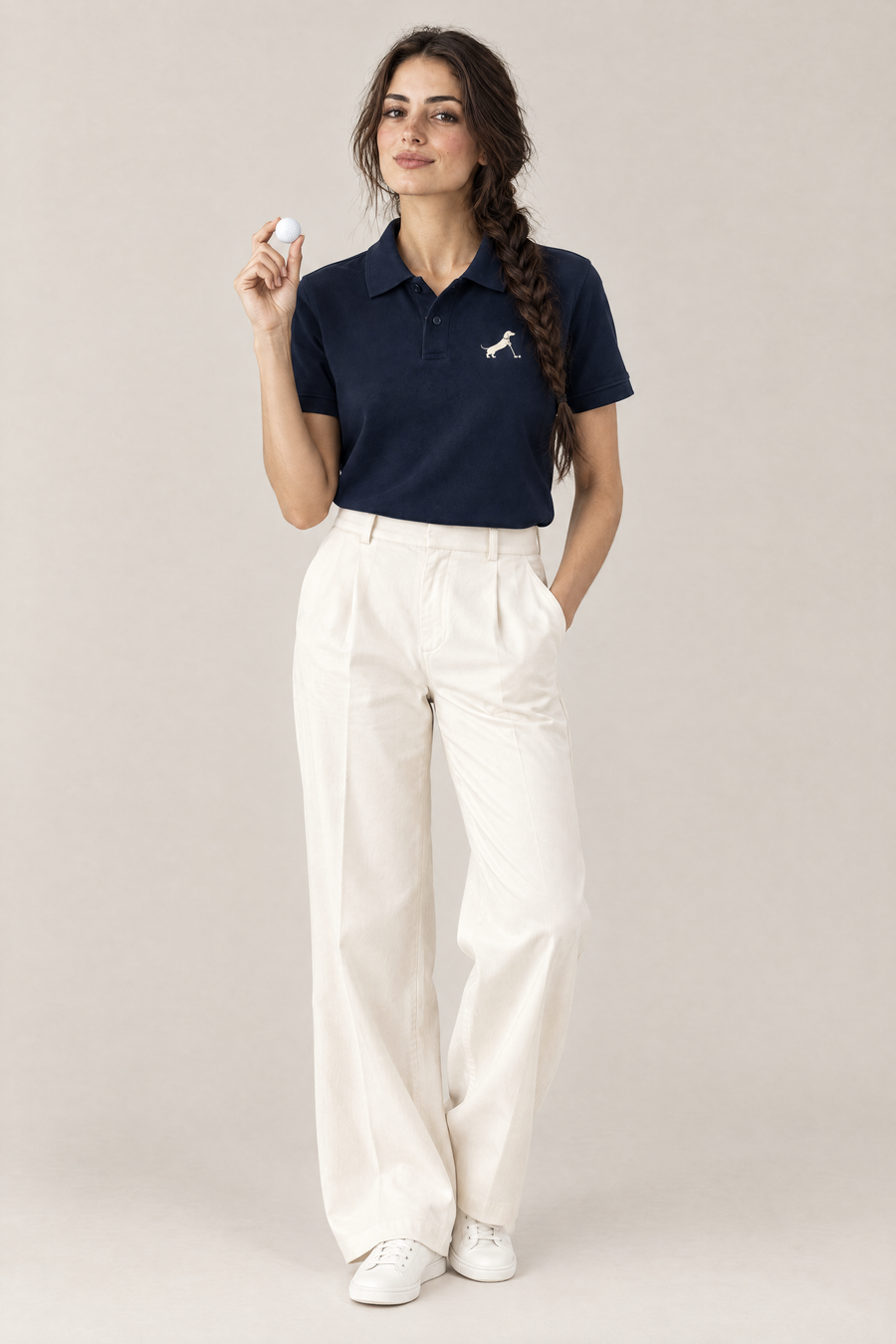 Woman holding a golf ball in navy blue Putting dachshund golf polo and cream wide-leg trousers, full-body studio look. Color: Navy Blue
