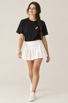Woman walking in black Putting dachshund golf t-shirt tucked into a white pleated skirt, three-quarter view. Color: Black