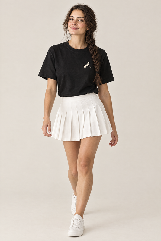 Woman walking in black Putting dachshund golf t-shirt tucked into a white pleated skirt, three-quarter view. Color: Black