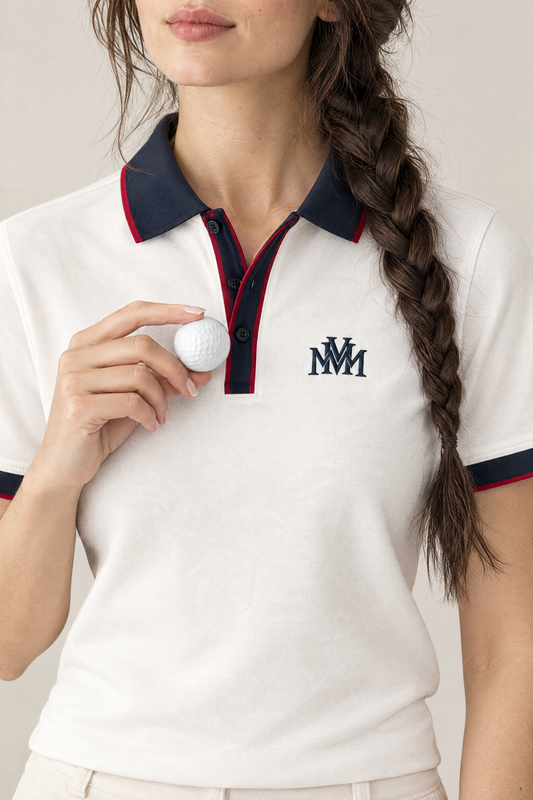 Woman holding a golf ball next to the navy MVM monogram on the white Club Crest polo, close-up. Color: White with Navy Blue