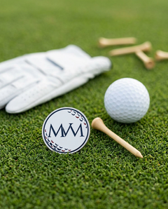 Pure Ball golf ball marker in navy and burgundy print on grass with a wooden tee and golf glove