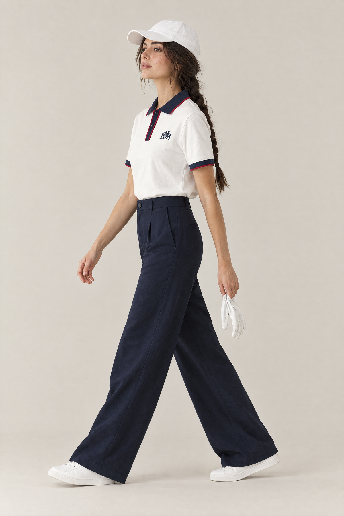 Woman in profile wearing the white Club Crest polo with navy wide-leg trousers and a white cap. Color: White with Navy Blue