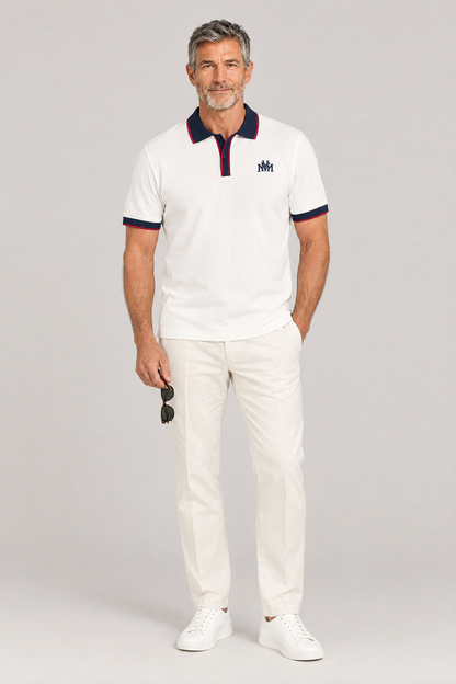 Man wearing the white Club Crest color block polo with navy trim, holding sunglasses, full body. Color: White with Navy Blue