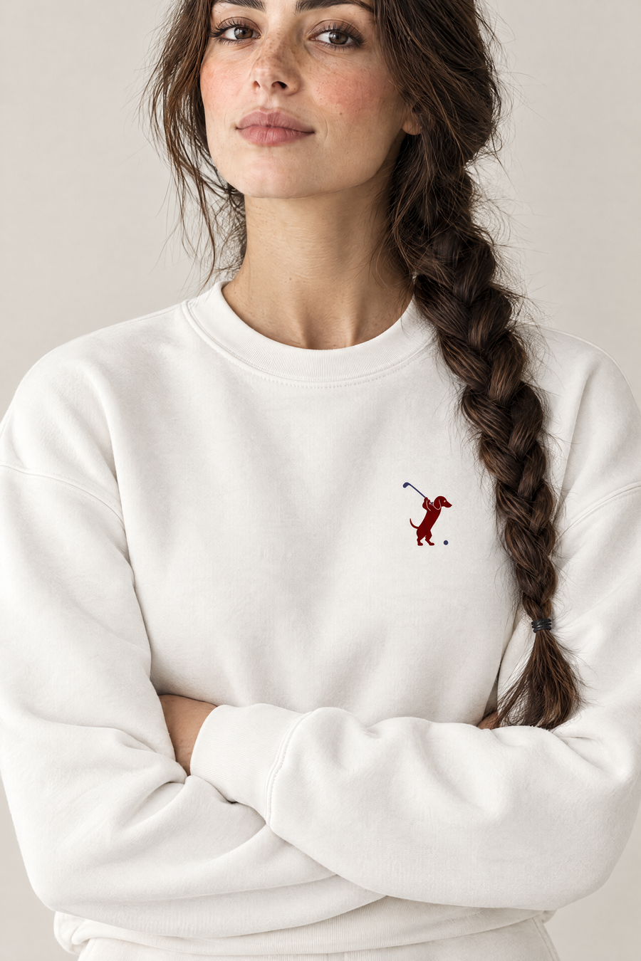 Close-up of woman with crossed arms wearing white Swing dachshund golf sweatshirt, chest print detail. Color: White