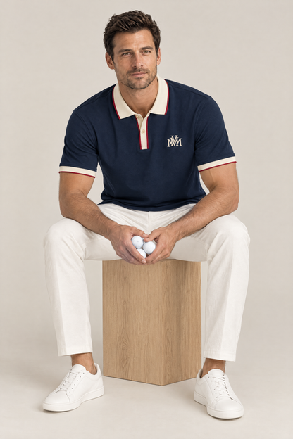 Man sitting on a wooden box in the navy Club Crest polo with apricot trim, holding golf balls. Color: Navy Blue with Apricot