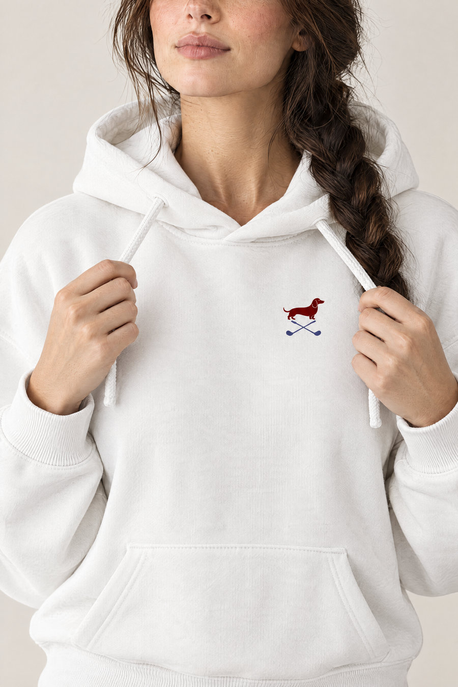Close-up of woman holding the drawstrings of a white Club & Swing dachshund golf hoodie, chest print detail. Color: White